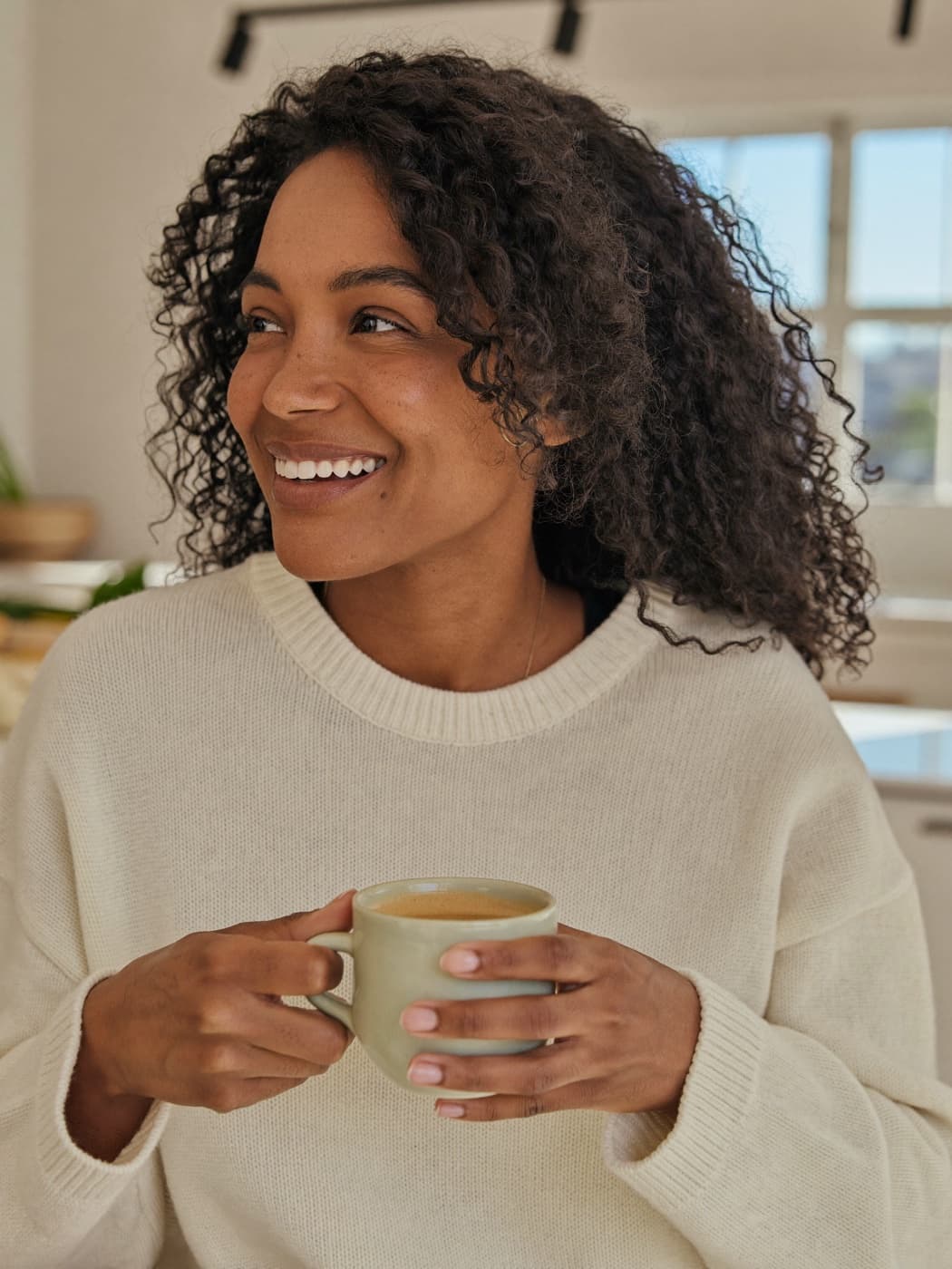 A woman smiling at home with a cup of coffee