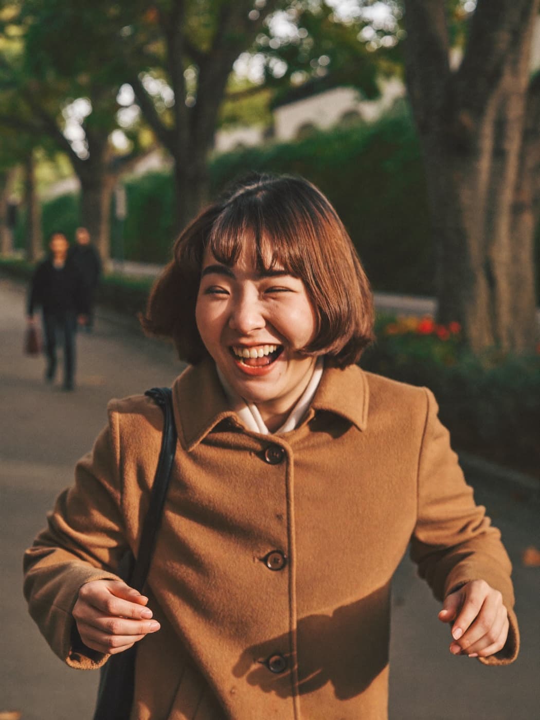 A woman laughing while walking outdoors on a tree-lined street